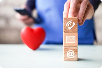 This is a picture of someone holding three blocks one has the phone logo, email logo, and the @ symbol, with a heart in the background.